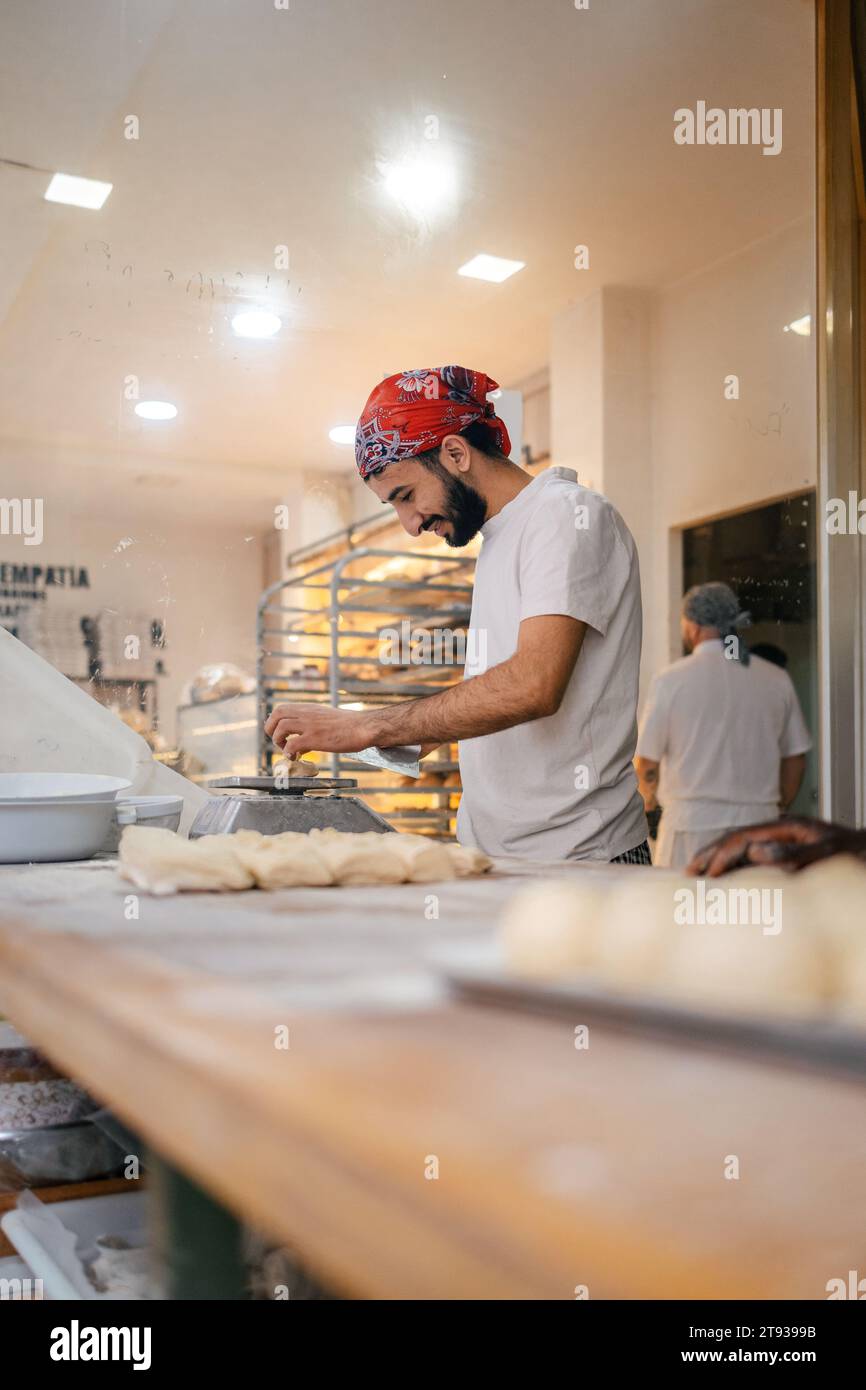Young arabic baker dressed with white clothes and a red hat cutting ...