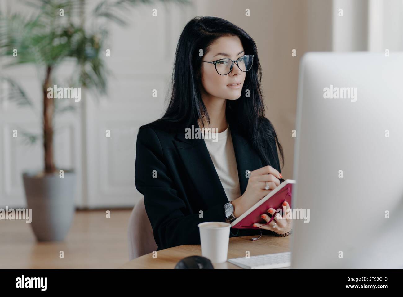 Concentrated journalist jotting down notes in a paper notepad, with computer and coffee in office Stock Photo