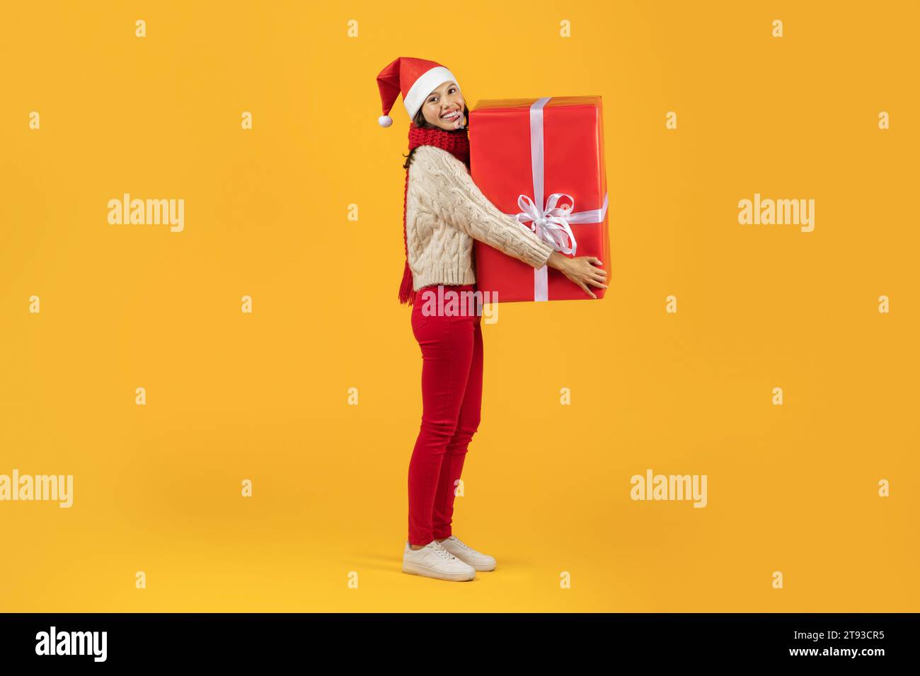 Happy lady in Christmas attire holds big holiday present, studio Stock