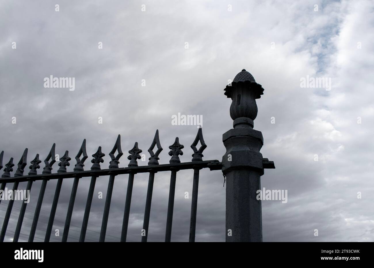 Wrought iron gate decorative fence post tops against dark stormy