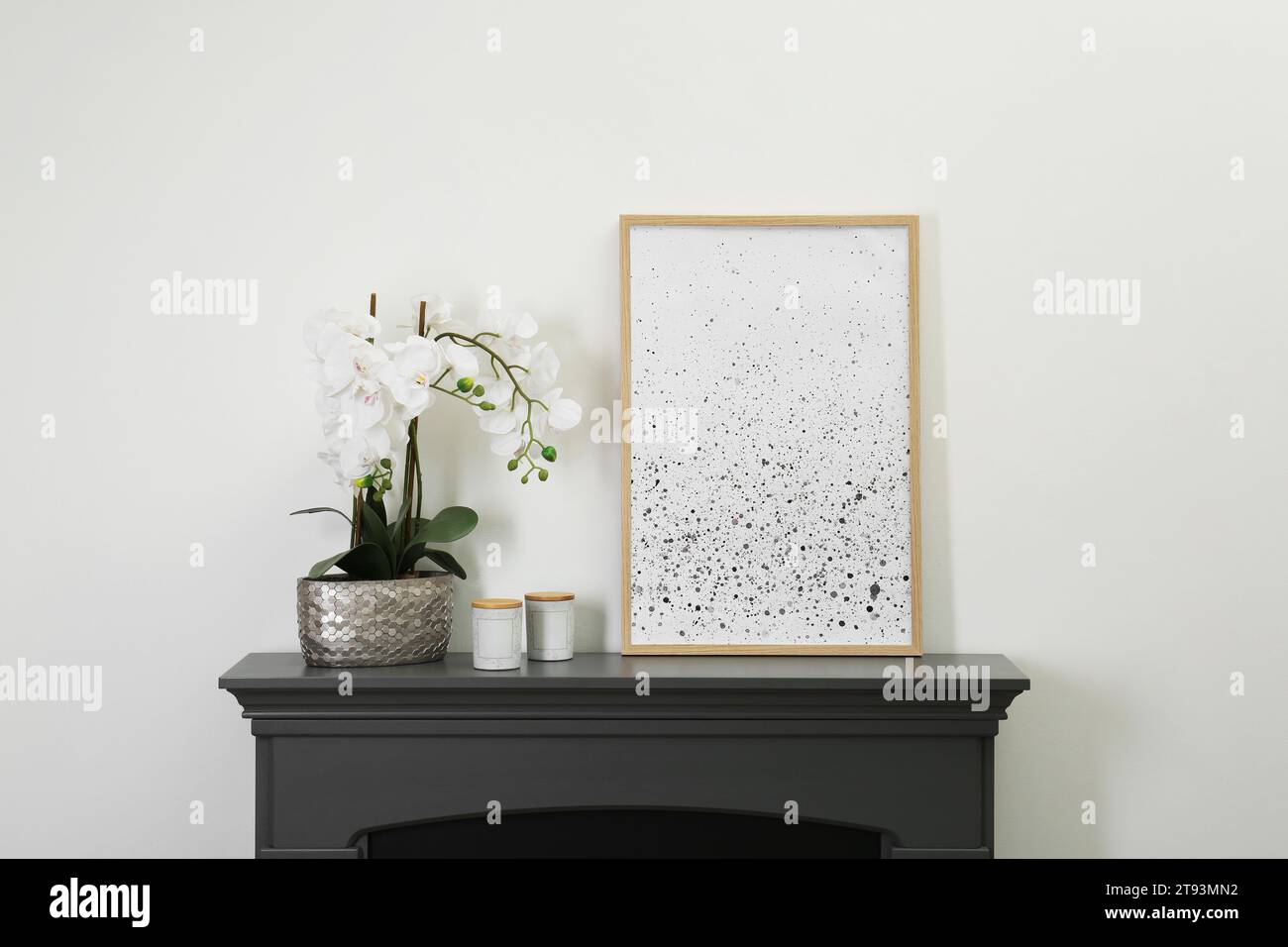Picture frame, candles and orchid on fireplace near white wall indoors. Interior element Stock Photo