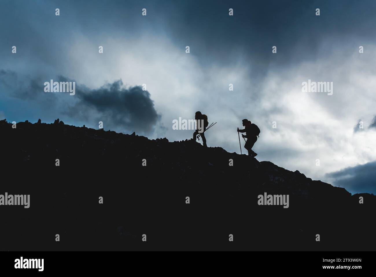 Underexposed photograph of two people in silhouette hiking up a mountain. couple ascending a mountain peak. sports and outdoor activities Stock Photo