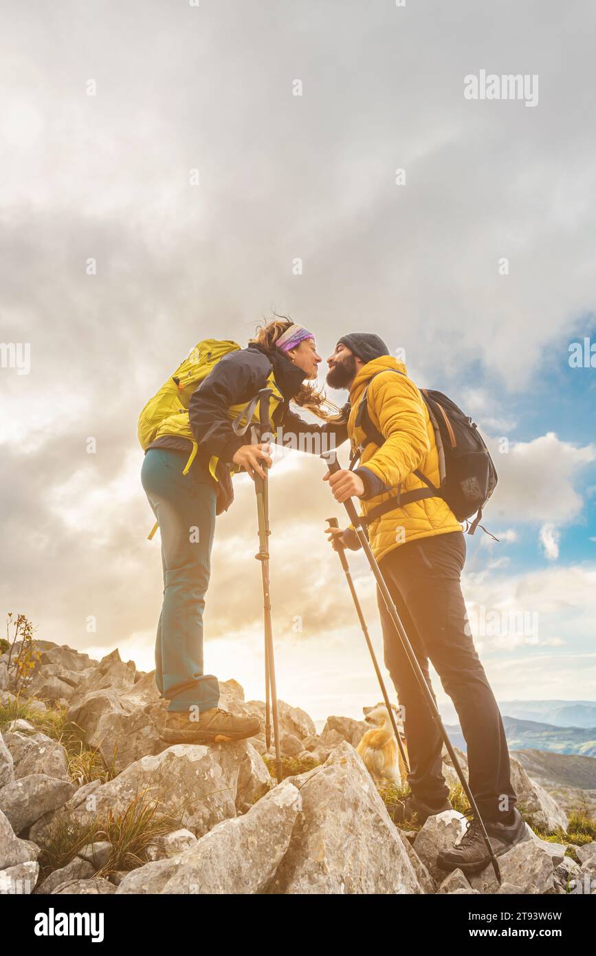 hiker couple kissing upon reaching the top of the mountain. two mountaineers hiking in the mountains with their dog. outdoor sports. Stock Photo