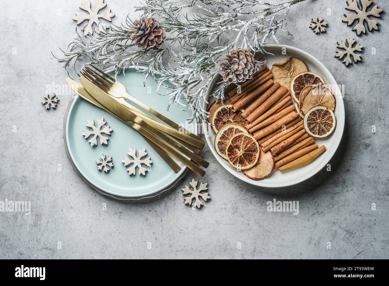 Christmas table setting with golden cutlery, pale blue plate, cinnamon sticks, dried orange natural dried apples and oranges and winter branches on gr Stock Photo
