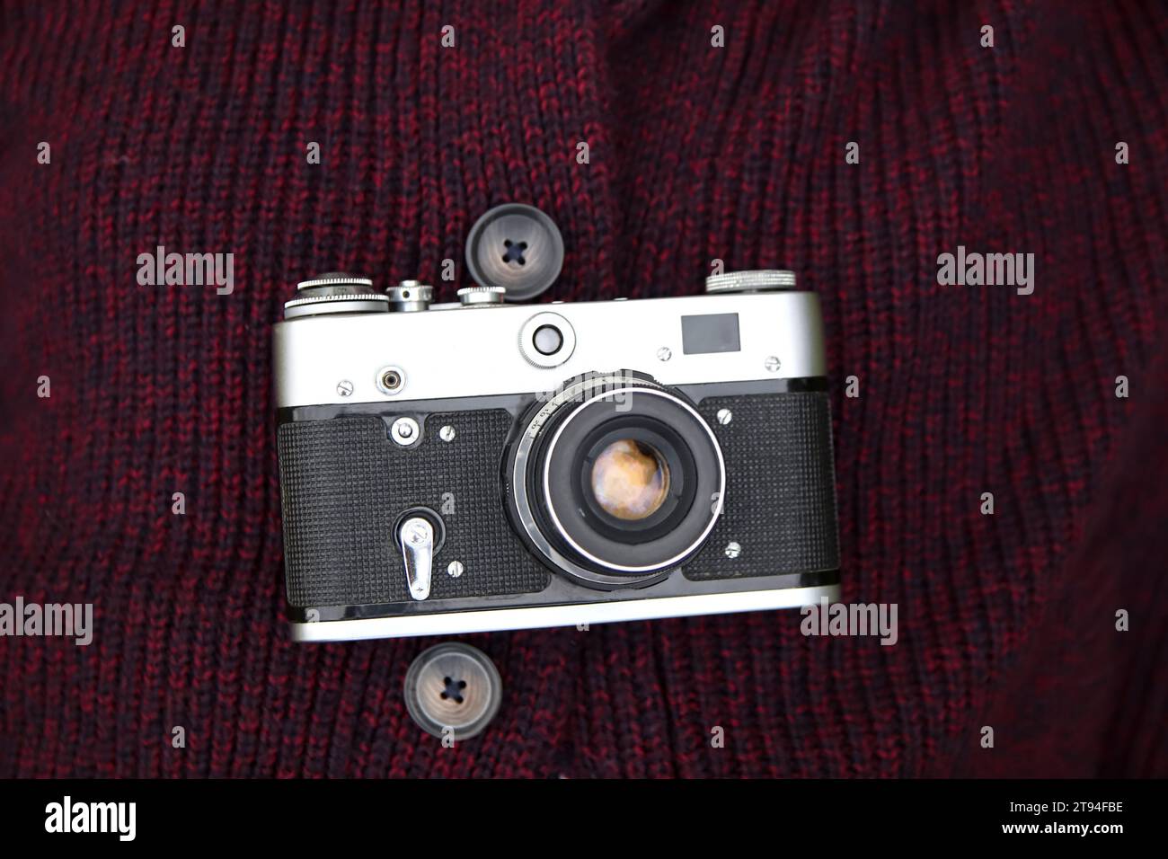 Retro film photo camera on red knitted sweater background. Old retro camera on vintage abstract background. Close up Stock Photo
