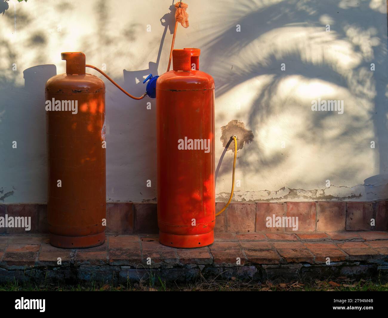 Two orange propane tanks against a wall illuminated by the light of the sunset, and the shadow of a palm tree, in a farm near the colonial town of Vil Stock Photo
