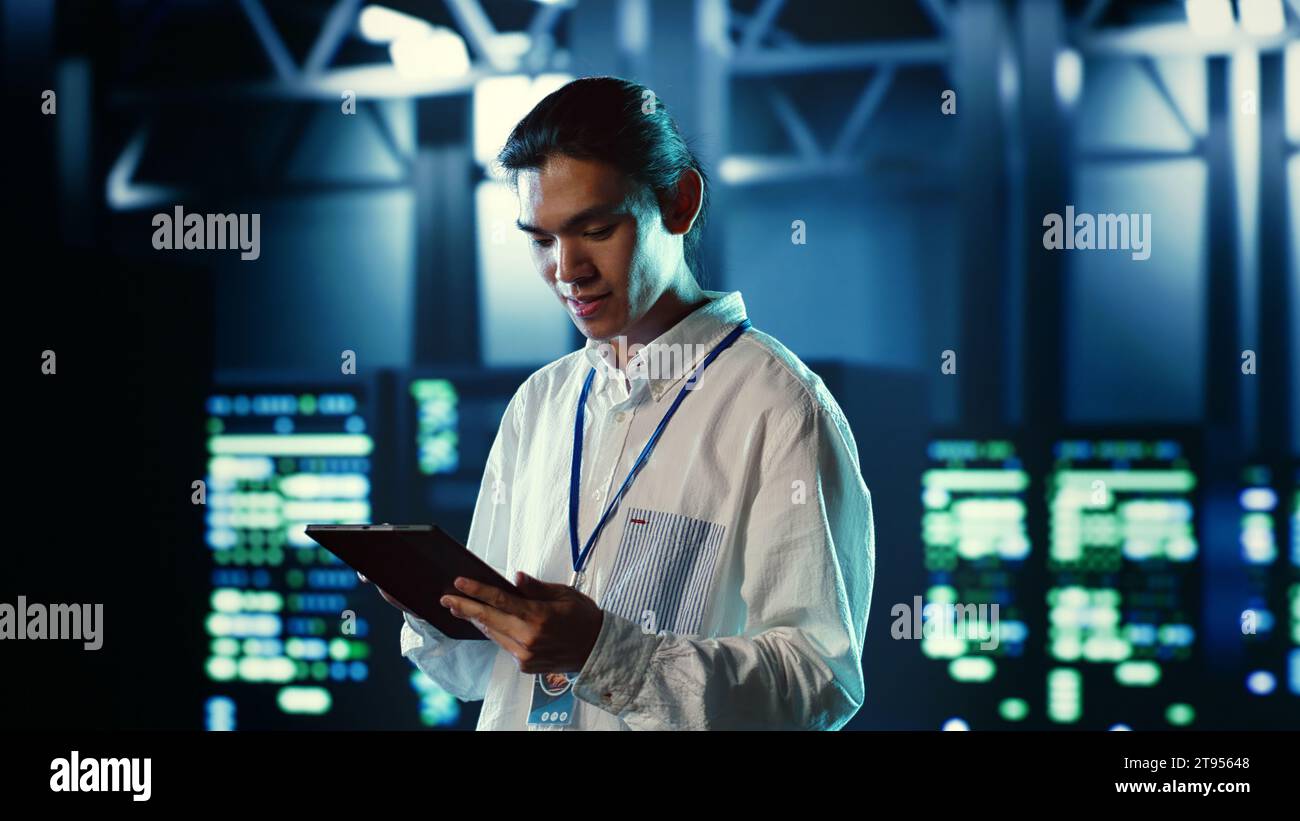 Proactive employee walking through data center electronics providing processing resources for different workloads. Organized engineer evaluating server rigs tasked with solving complex operations Stock Photo