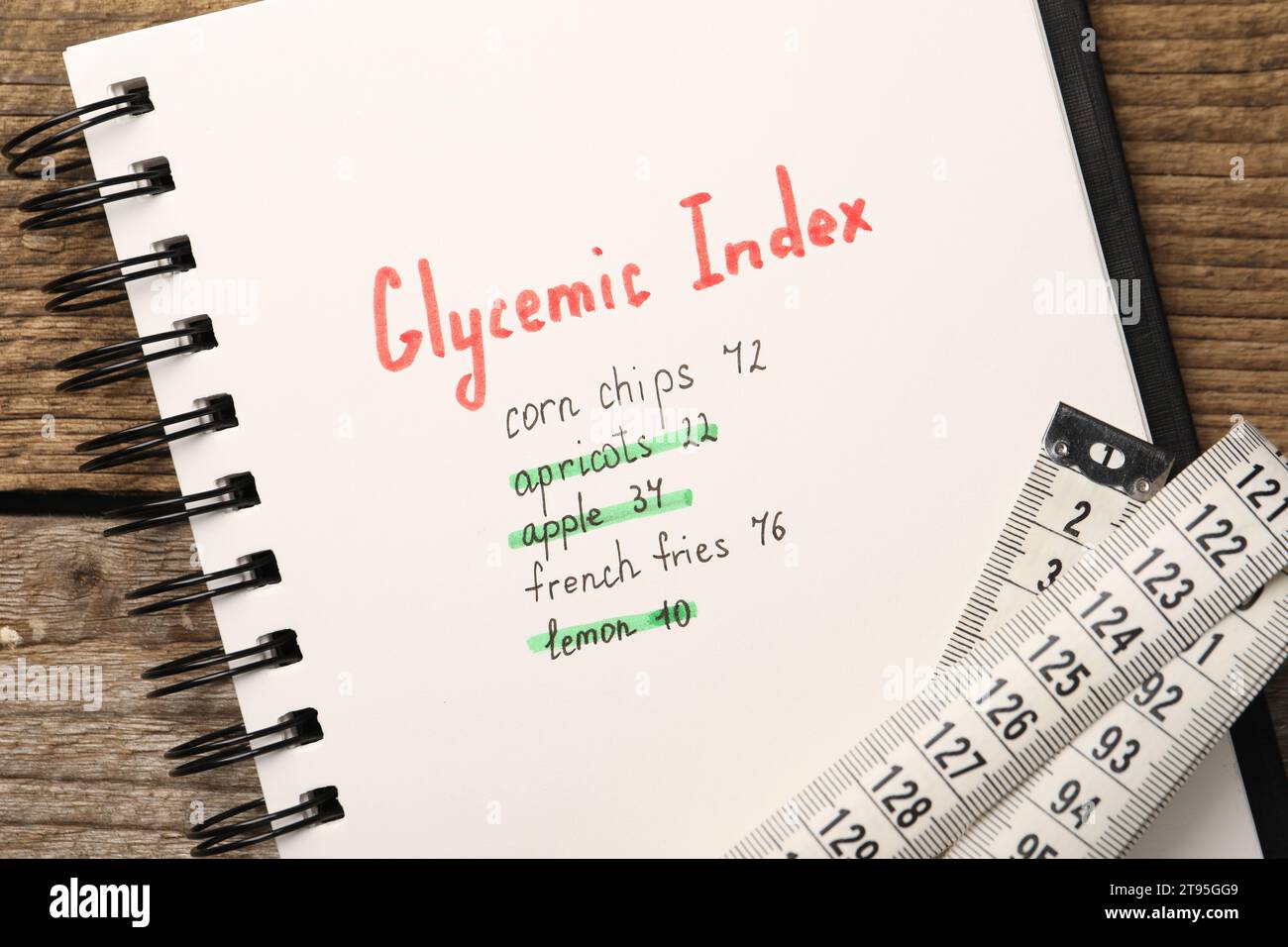 Glycemic Index. Notebook with information and measuring tape on wooden table, top view Stock Photo
