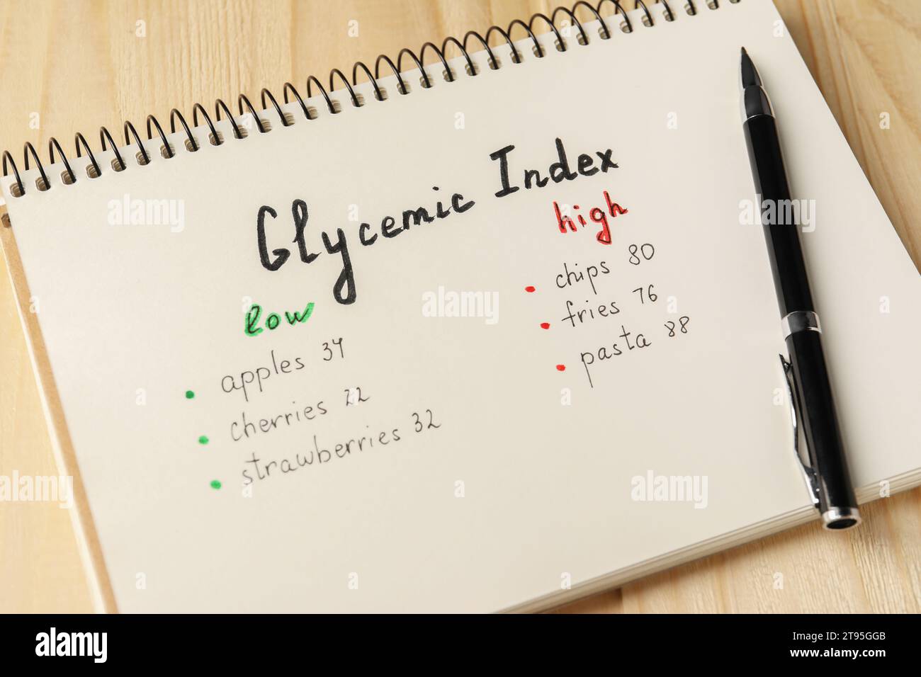 List with products of low and high glycemic index in notebook and pen on wooden table, closeup Stock Photo
