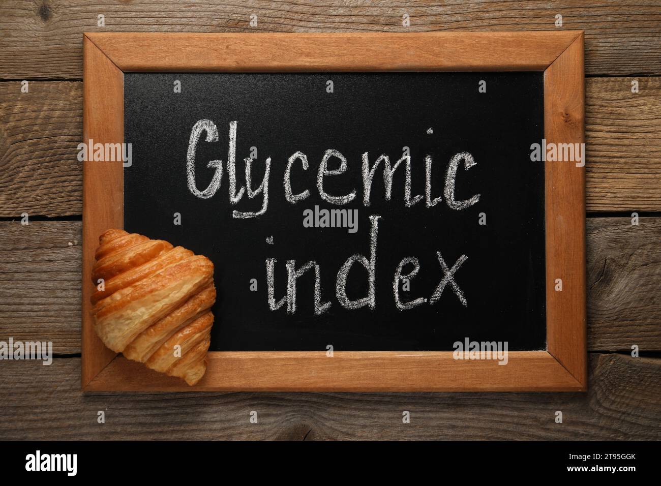 Small chalkboard with words Glycemic Index and croissant on wooden table, top view Stock Photo