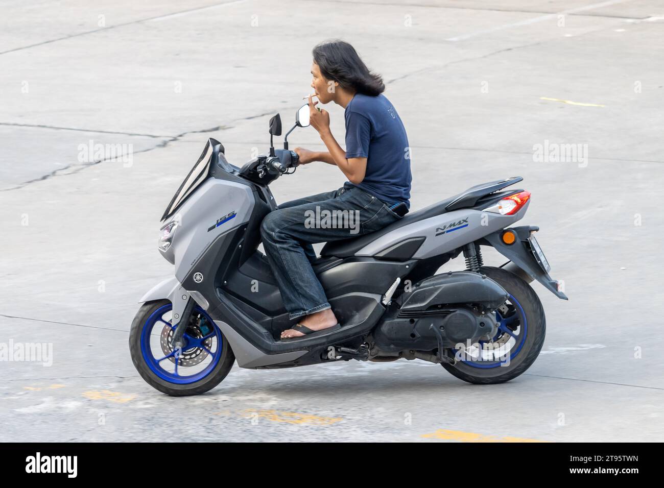 SAMUT PRAKAN, THAILAND, NOV 03 2023, A young man is riding a motorcycle and smoking a cigarette Stock Photo