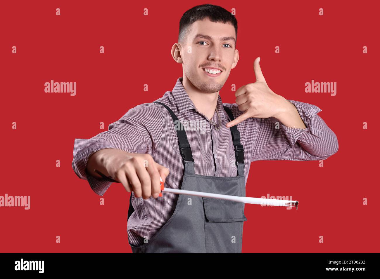 Male builder with tape measure showing "call me" gesture on red background Stock Photo