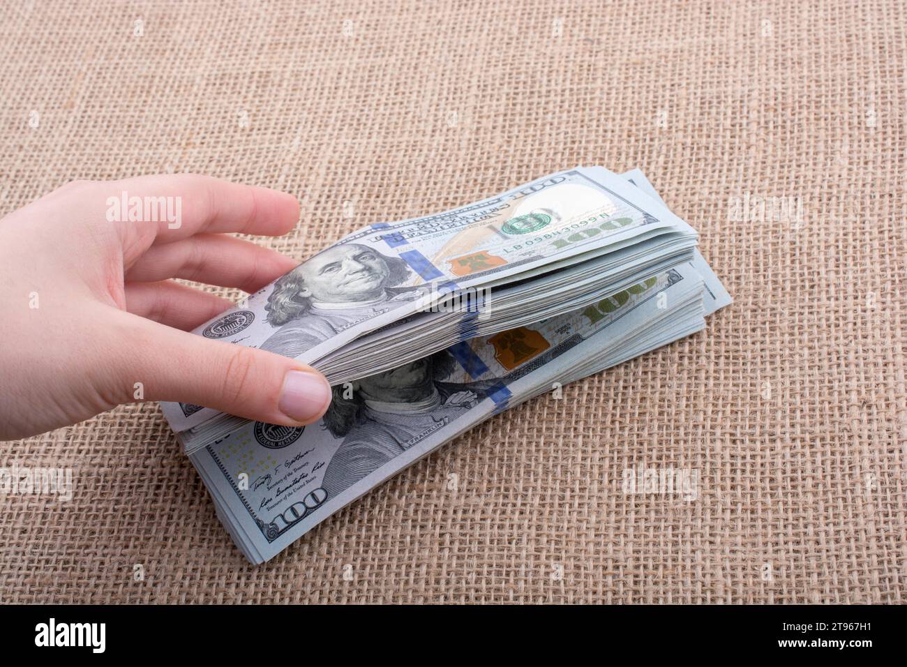 Hand holding banknote bundle of US dollar on a linen canvas background ...