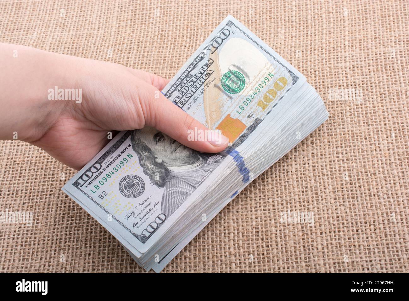 Hand holding banknote bundle of US dollar on a linen canvas background ...