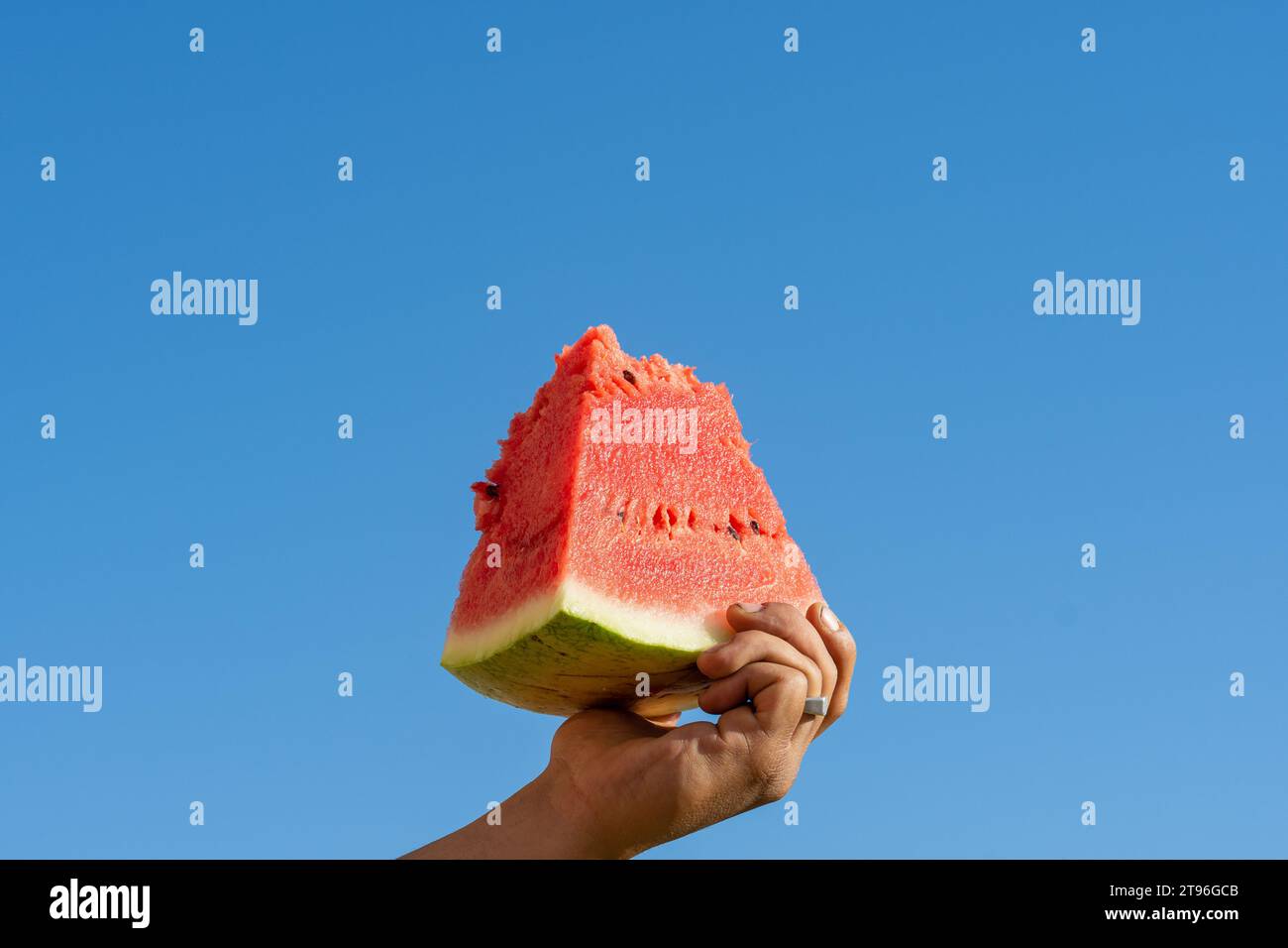 Close-up of a hand holding a slice of watermelon against a blue sky. Sign of resistance. Stock Photo