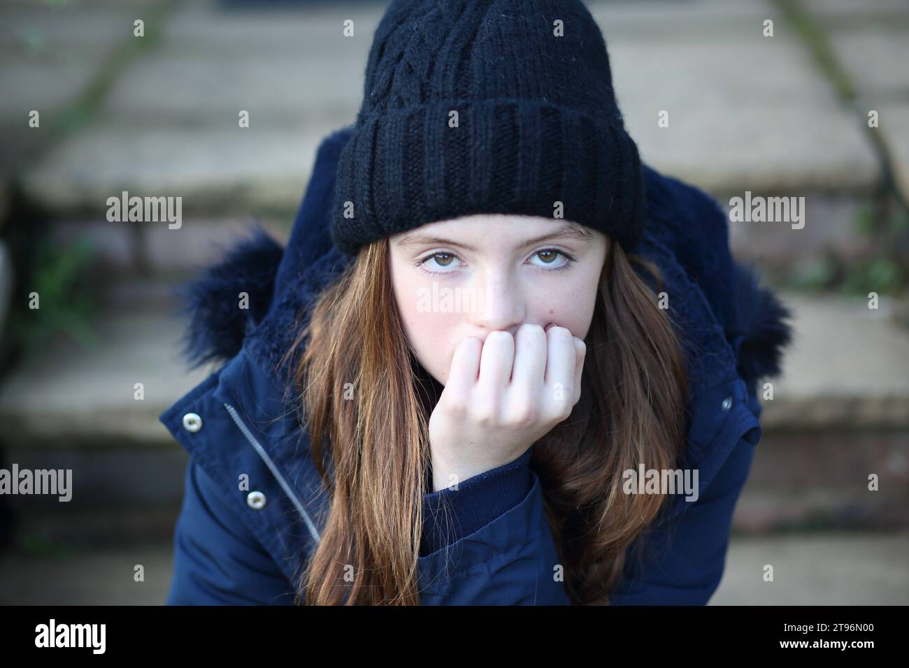 Girl sitting on step with eyes looking up, showing anxiety, staring at camera, strong eye contact Stock Photo