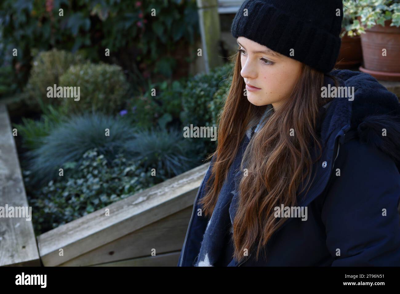 Girl sitting on step wearing woolly hat and coat and scarf trying to keep warm Stock Photo
