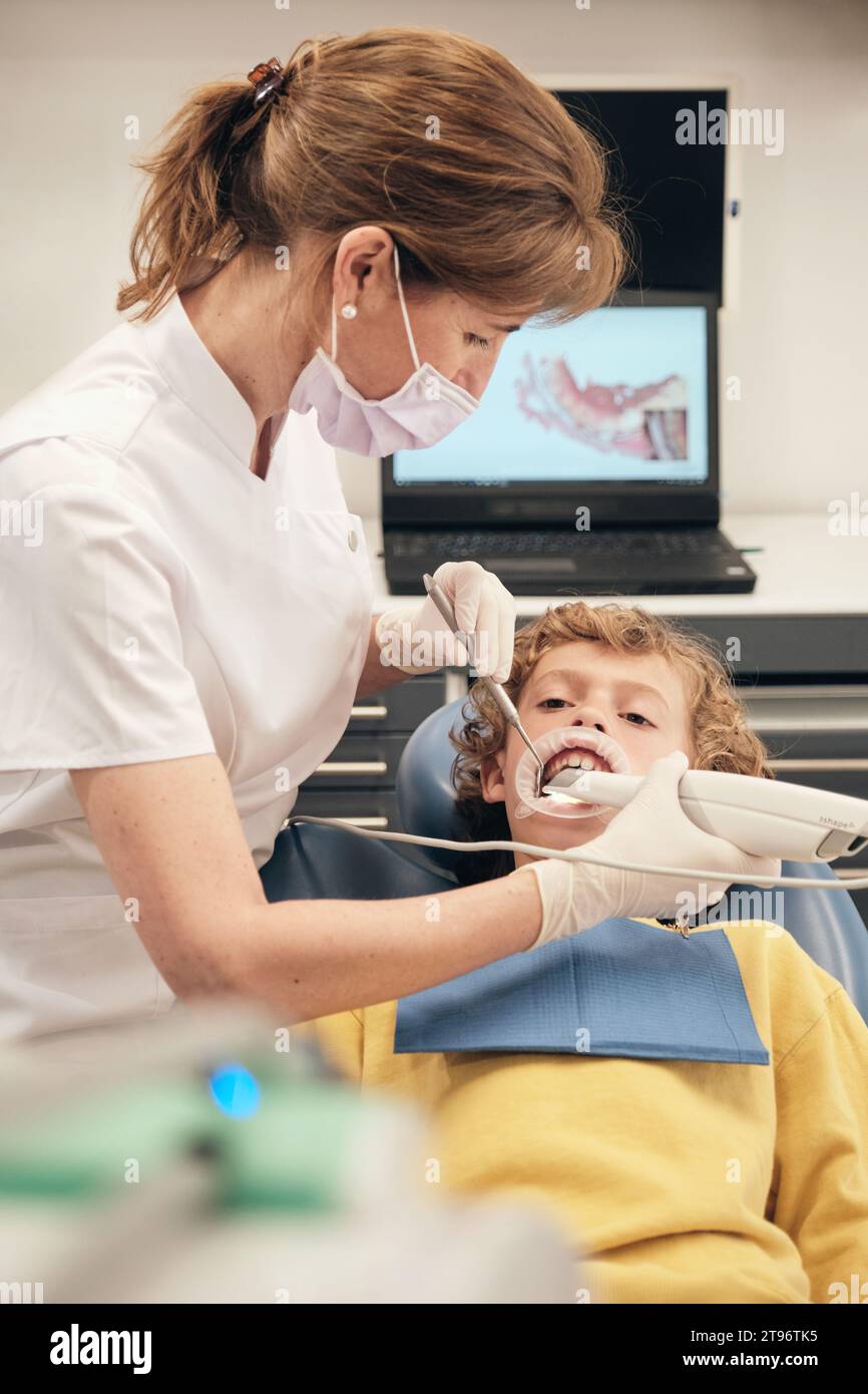 Side view of professional female dentist in mask and uniform robe applying intraoral scanner for