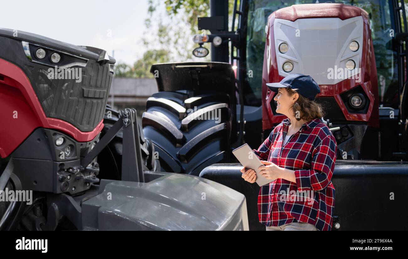 Female farmer with a digital tablet next to agricultural tractor. Stock Photo