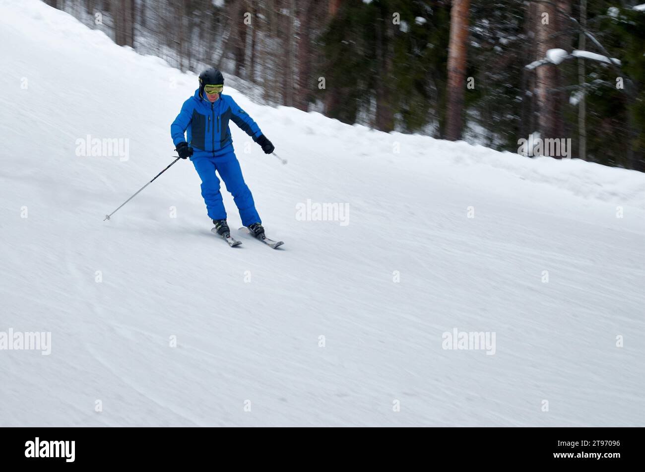 A man in blue sportswear on skis rides down a snowy slope Stock Photo