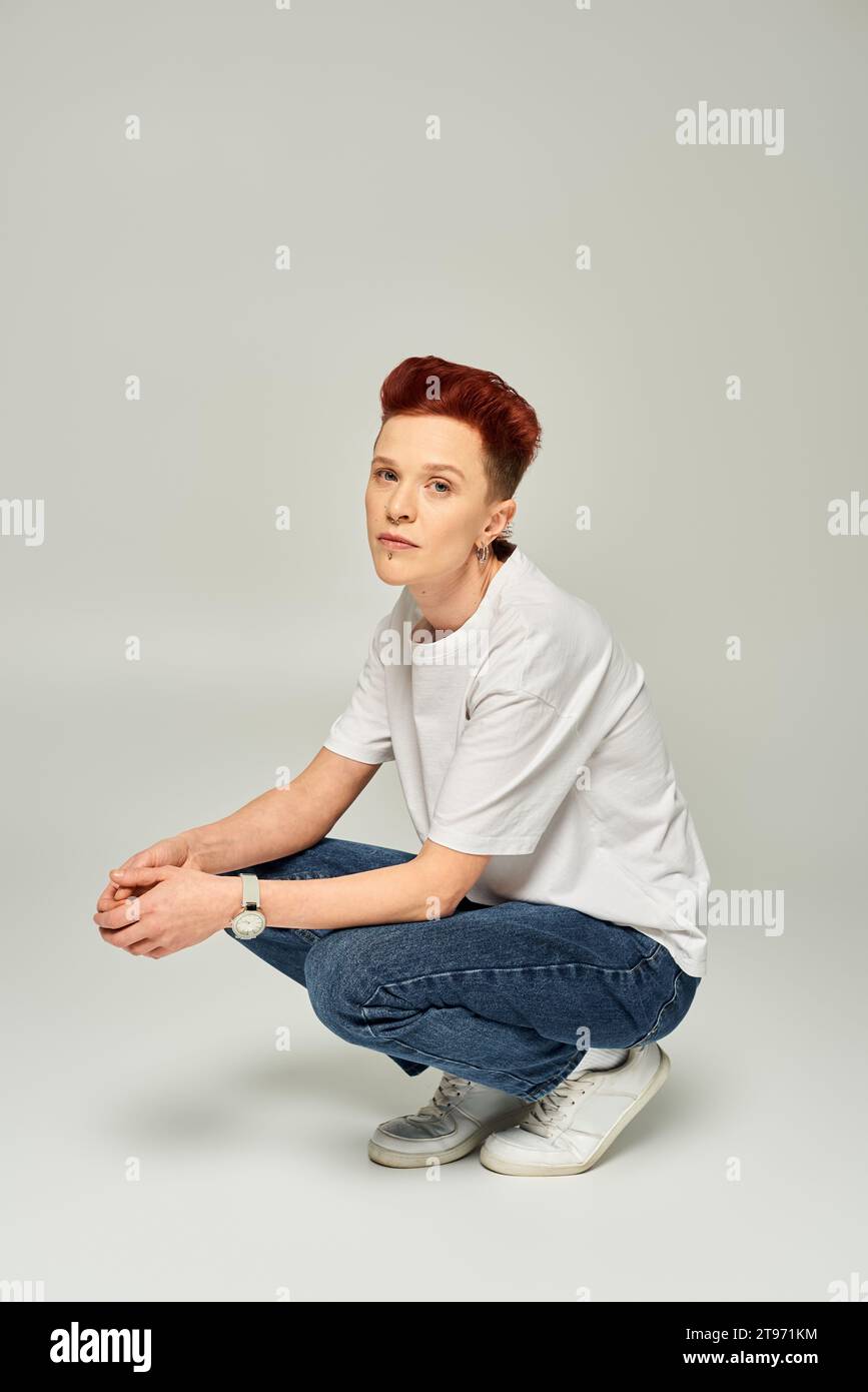 redhead-queer-person-in-white-t-shirt-and-jeans-sitting-on-haunches-and