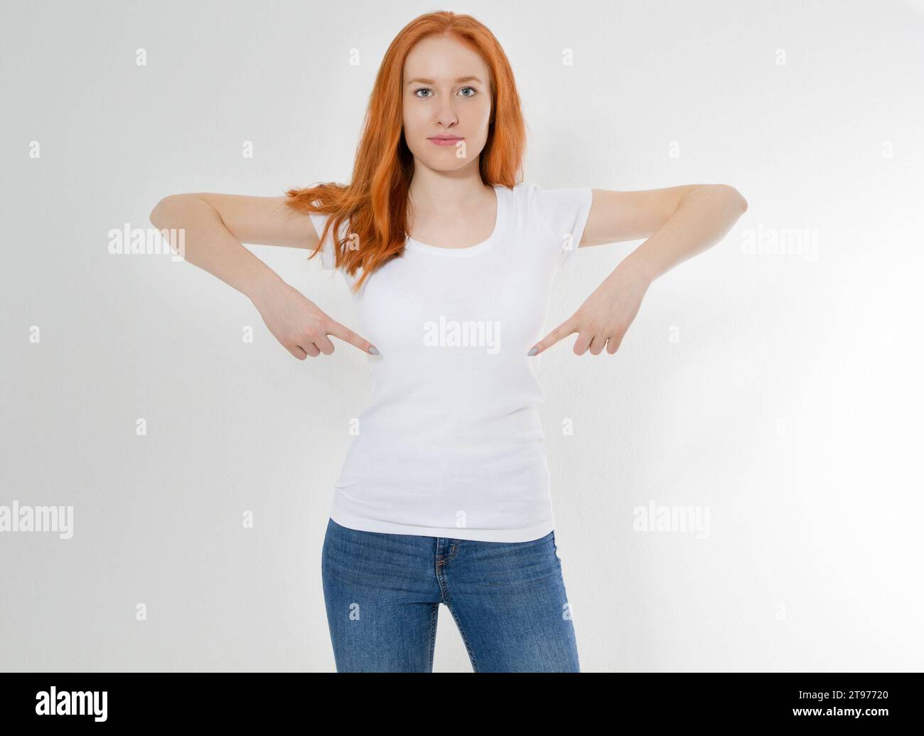 T-shirt design and advertising concept. Style and fashion. Indoor shot of cheerful smiling youngred head woman with red hair pointing index finger at Stock Photo