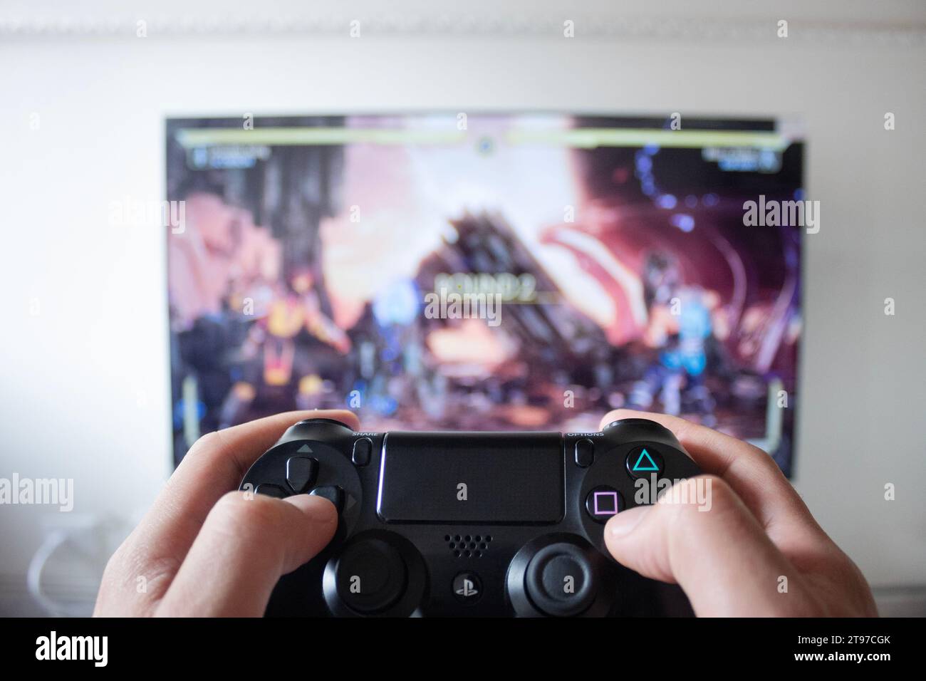 A male hand holding a play station 4 controller with fighter video game in a smart tv at background Stock Photo