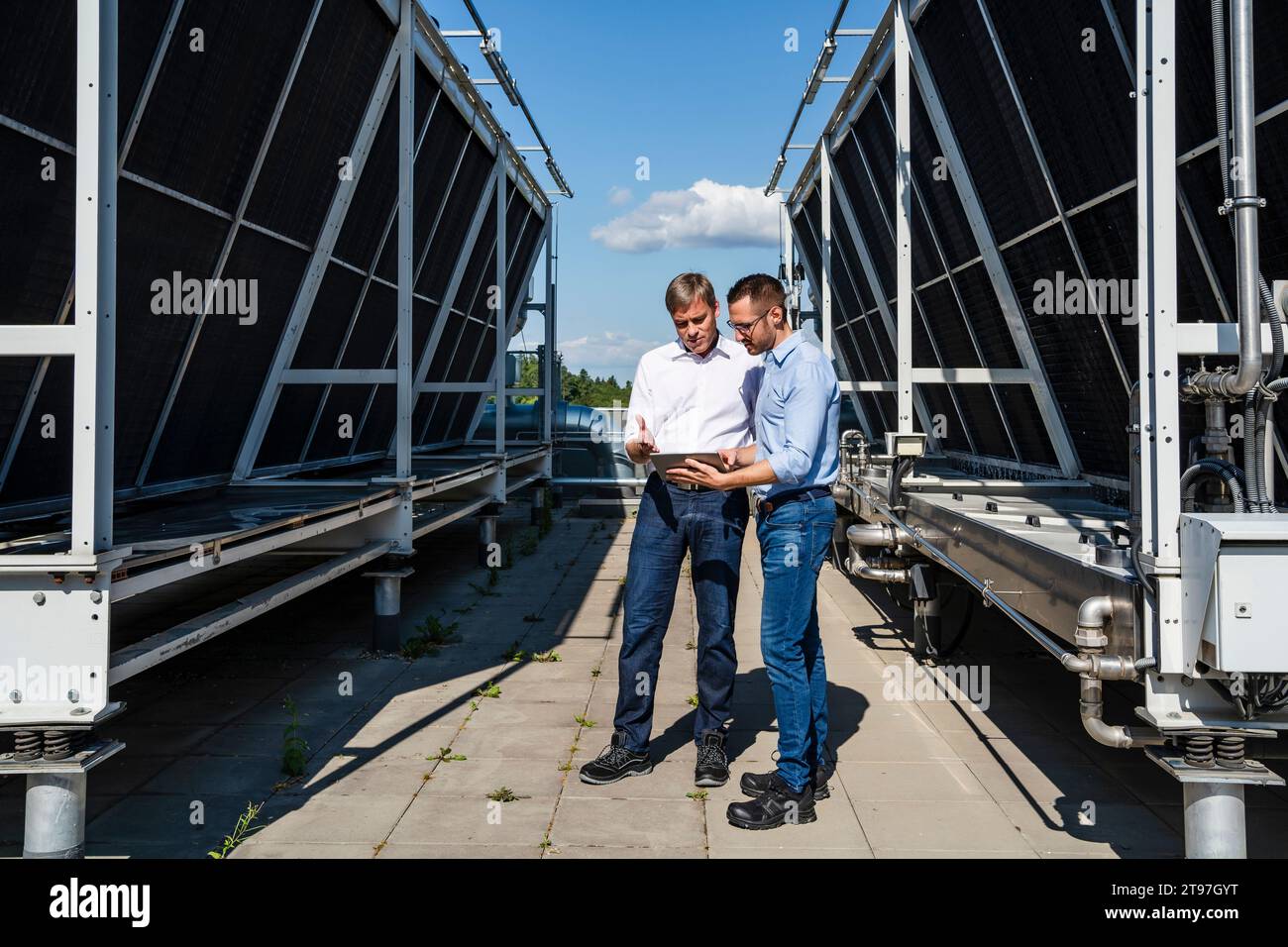 Two businessmen using digital tablet on rooftop beside refrigeration installation Stock Photo