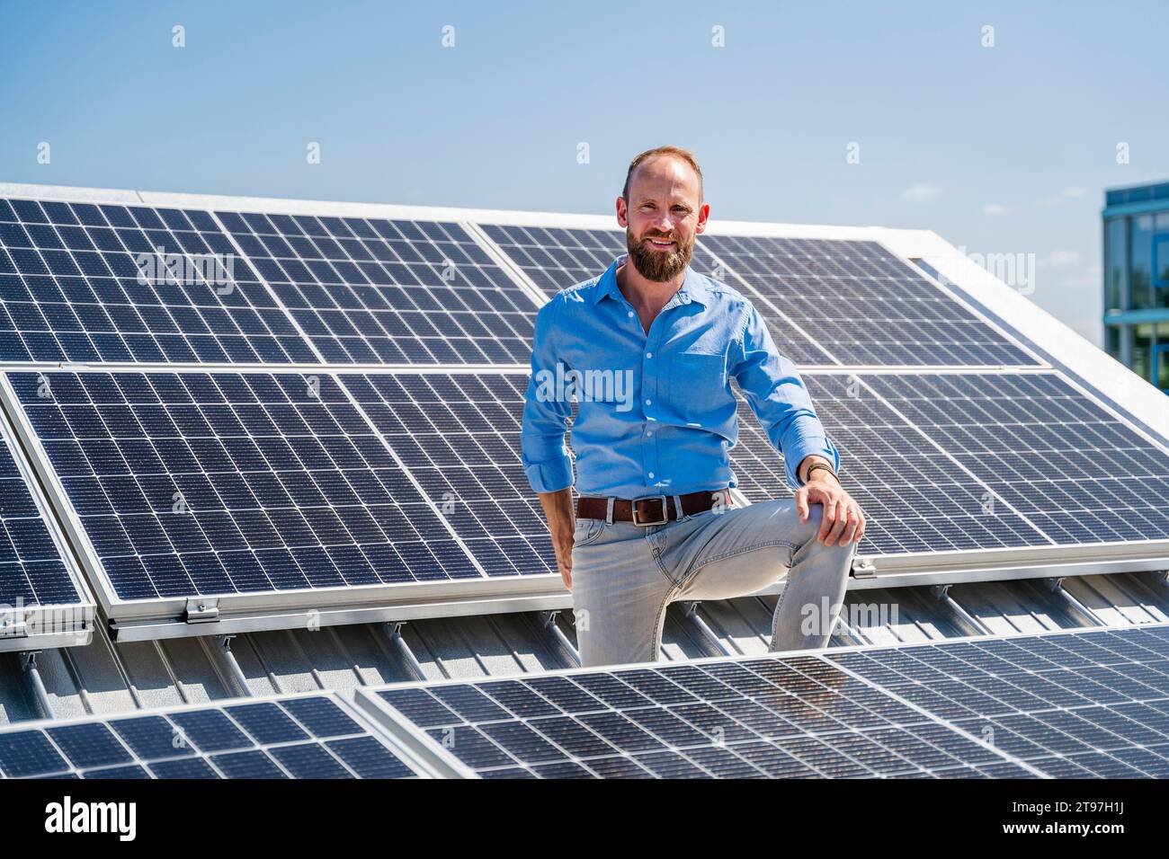 A cheerful businessman stands surrounded by solar panels, showcasing his commitment to sustainable energy Stock Photo