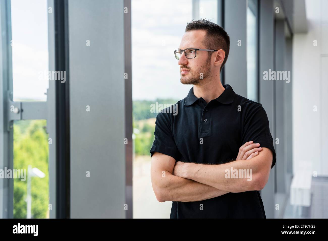 Contemplating businessman looking out of window with arms crossed Stock Photo