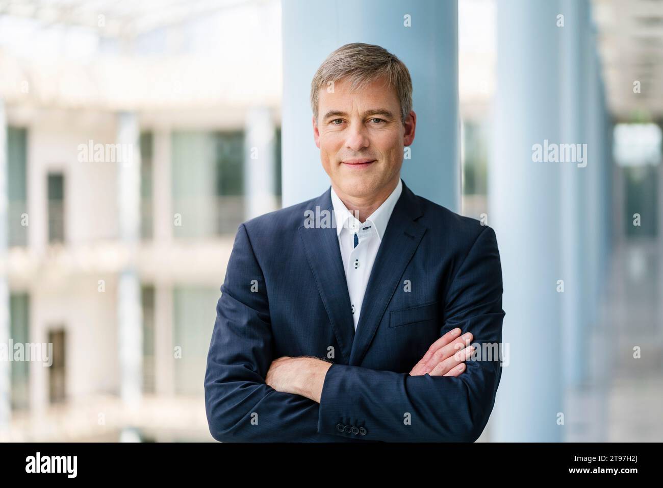 Successful businessman standing with arms crossed in front of column ...