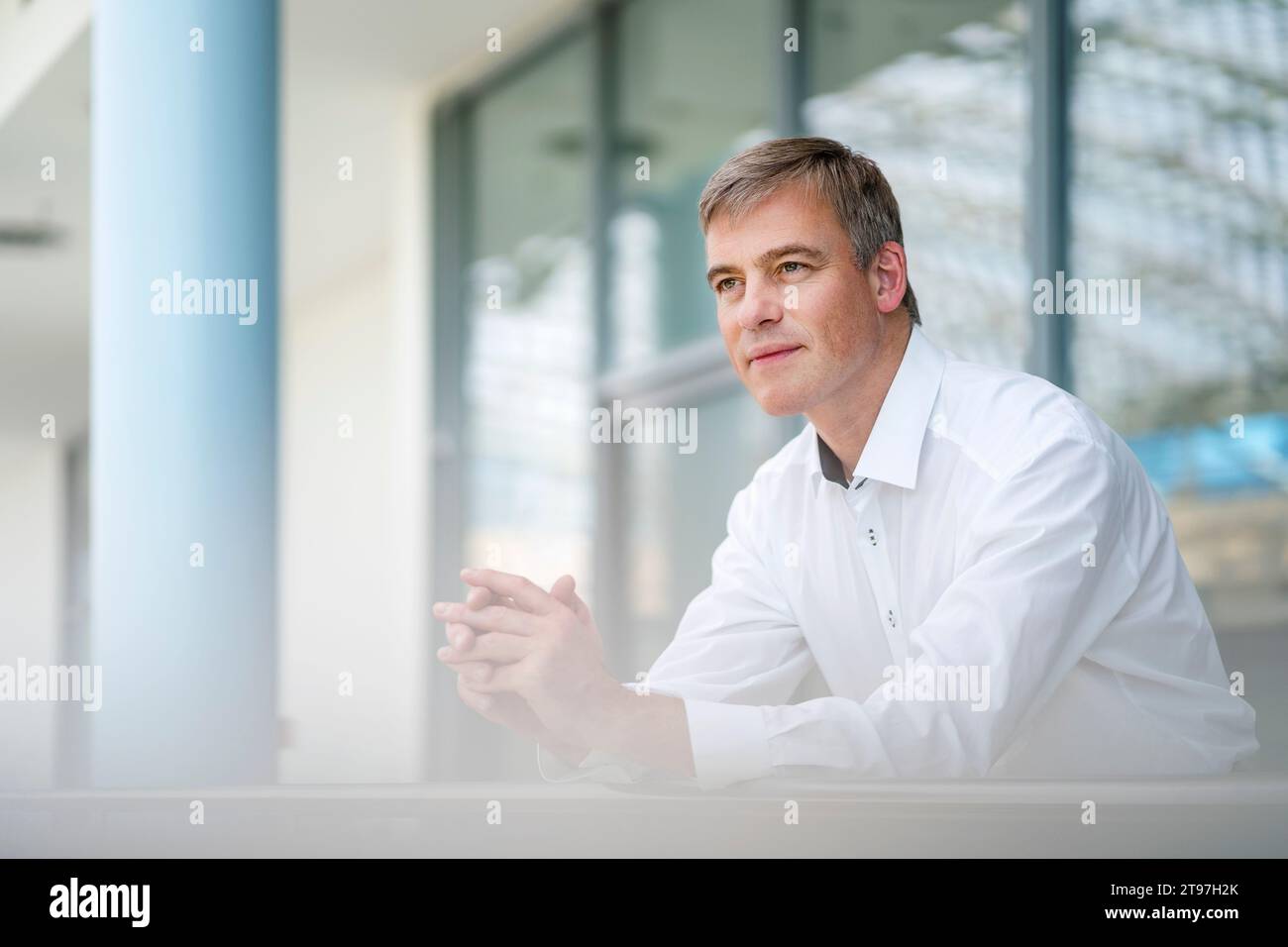 Serene businessman leaning on railing in office building Stock Photo