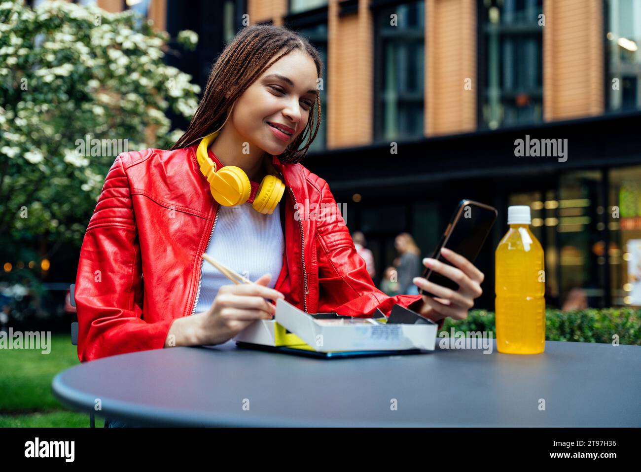 Smiling woman using mobile phone and having sushi on table at sidewalk cafe Stock Photo
