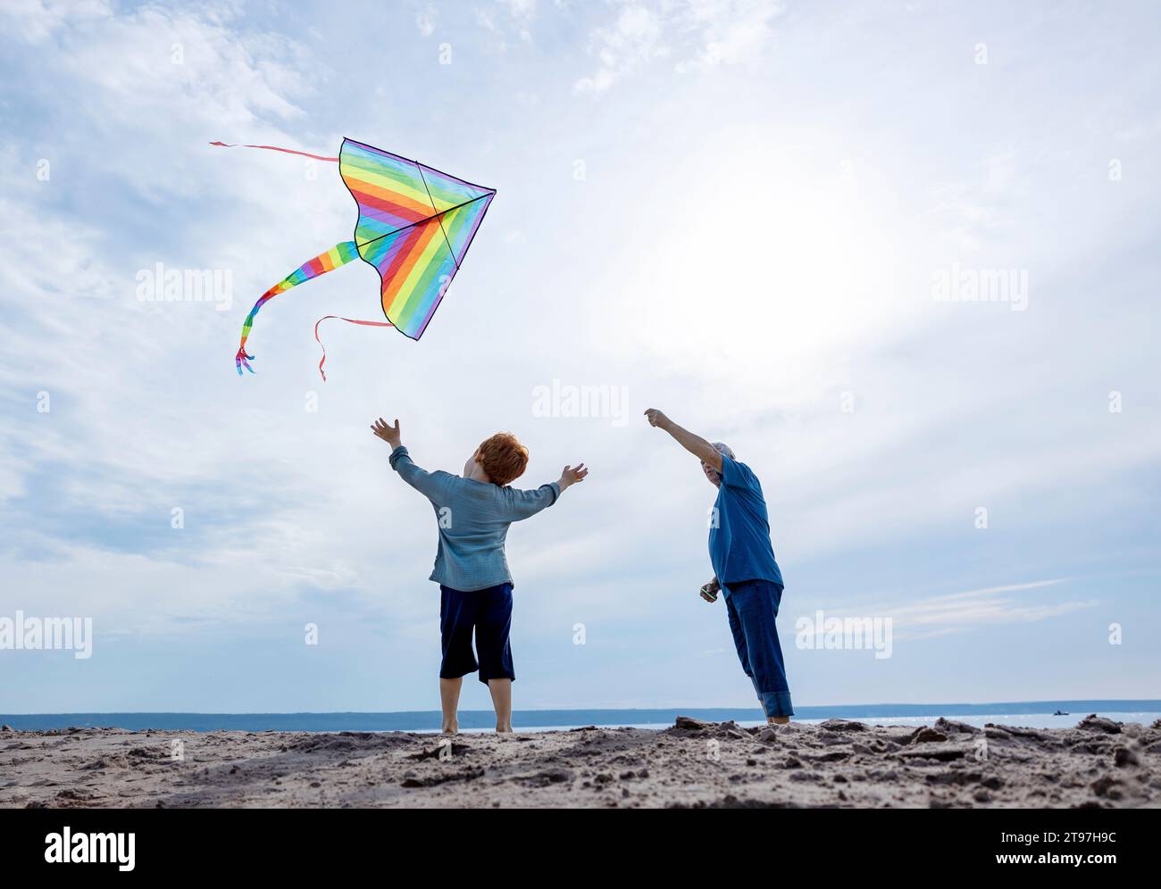 Boy standing with grandfather flying kite at beach Stock Photo