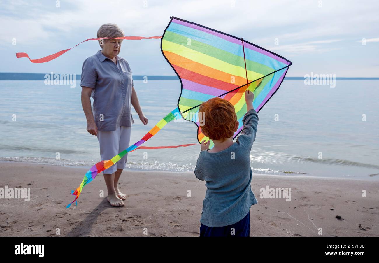 Boy holding colorful kite with grandmother near shore at beach Stock Photo