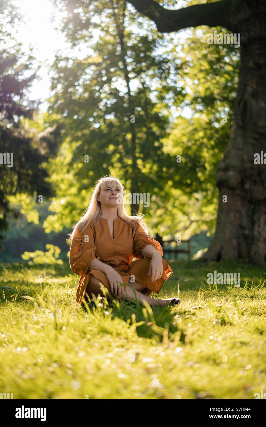 Contemplative woman sitting on grass in park Stock Photo