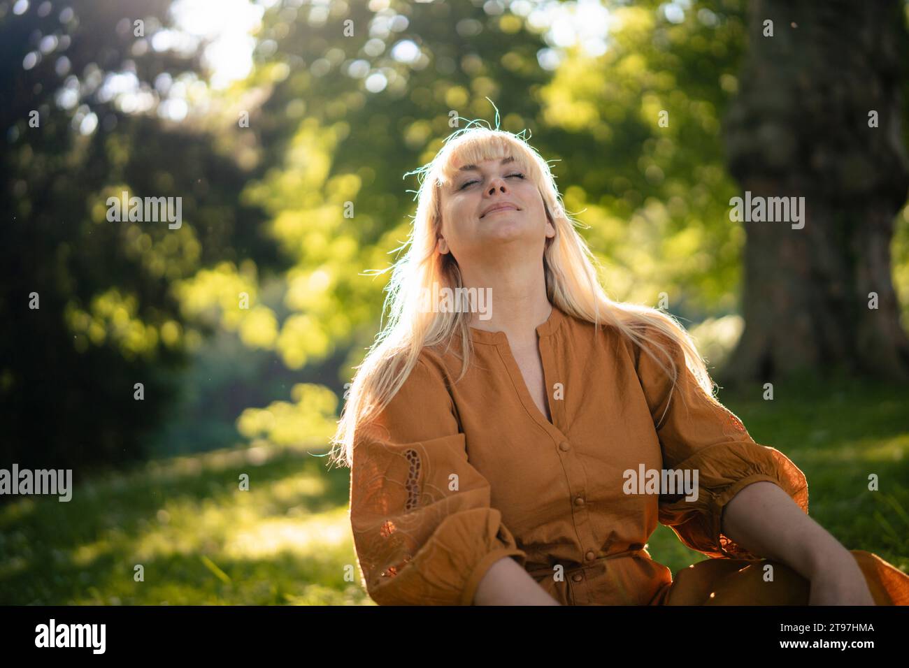 Blond woman sitting with eyes closed in park Stock Photo - Alamy