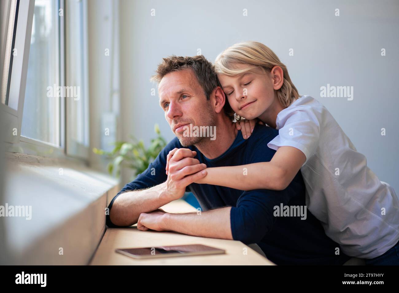 Contemplative father looking through window and holding hands with son at home Stock Photo