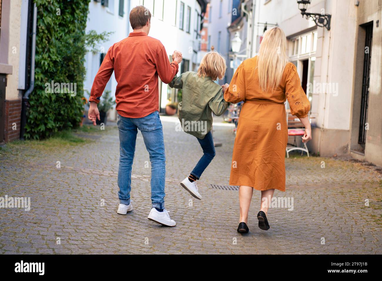 Parents holding hands and lifting son on alley Stock Photo