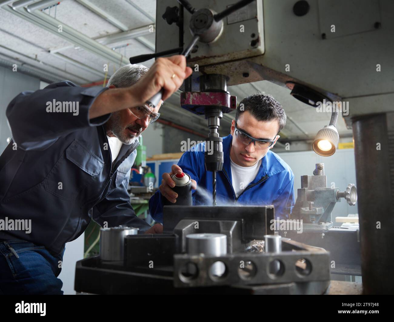 Instructor assisting trainee spraying lubricant on machine in workshop Stock Photo