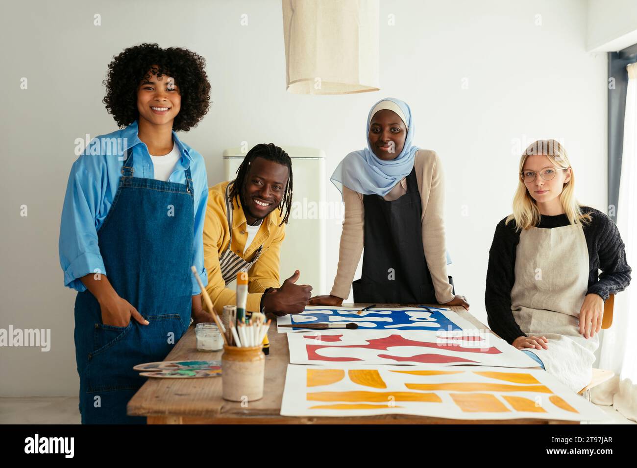 Smiling artists around desk with paintings in studio Stock Photo