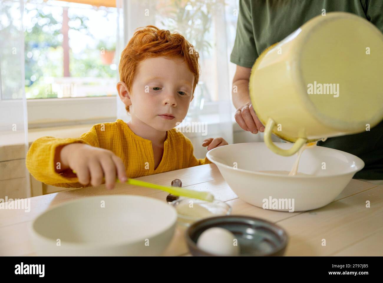 Grandmother pouring batter in bowl with grandson at table Stock Photo