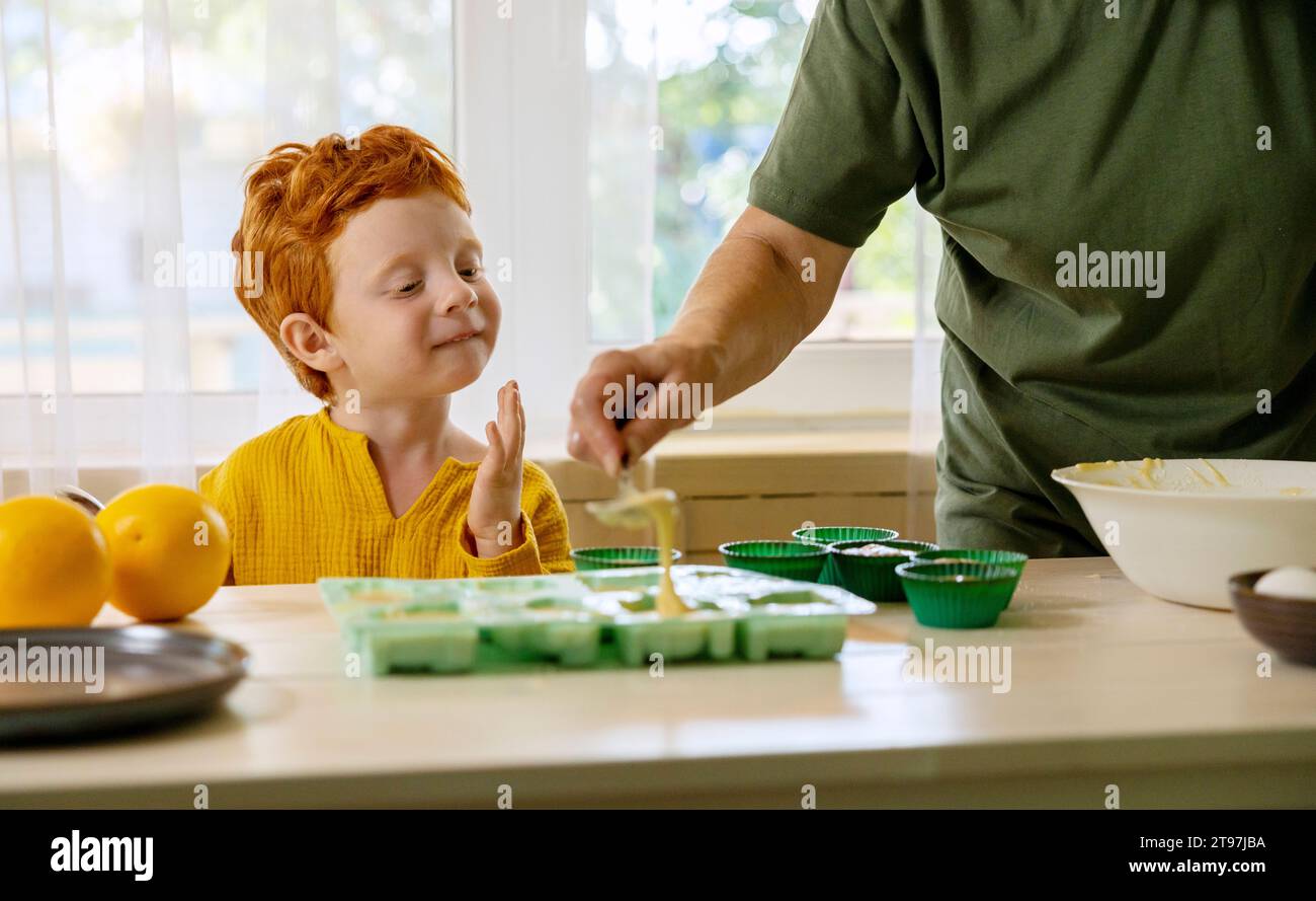 Grandmother putting cupcake batter in molds with grandson at kitchen Stock Photo