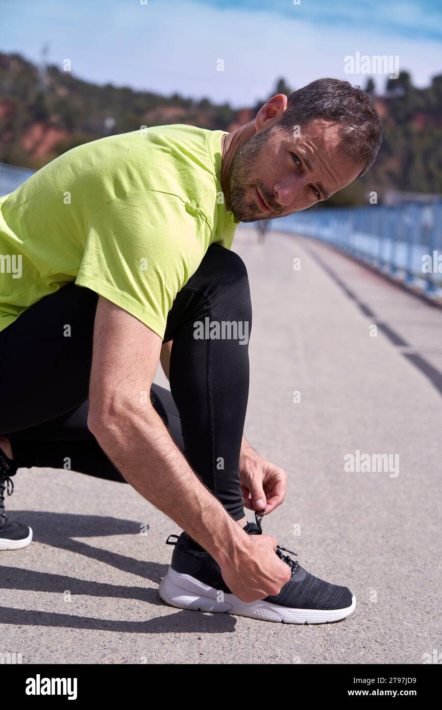 Man crouching and tying shoelace on sunny day Stock Photo
