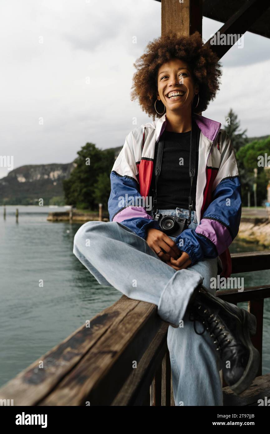 Happy young woman sitting on railing near lake Stock Photo - Alamy