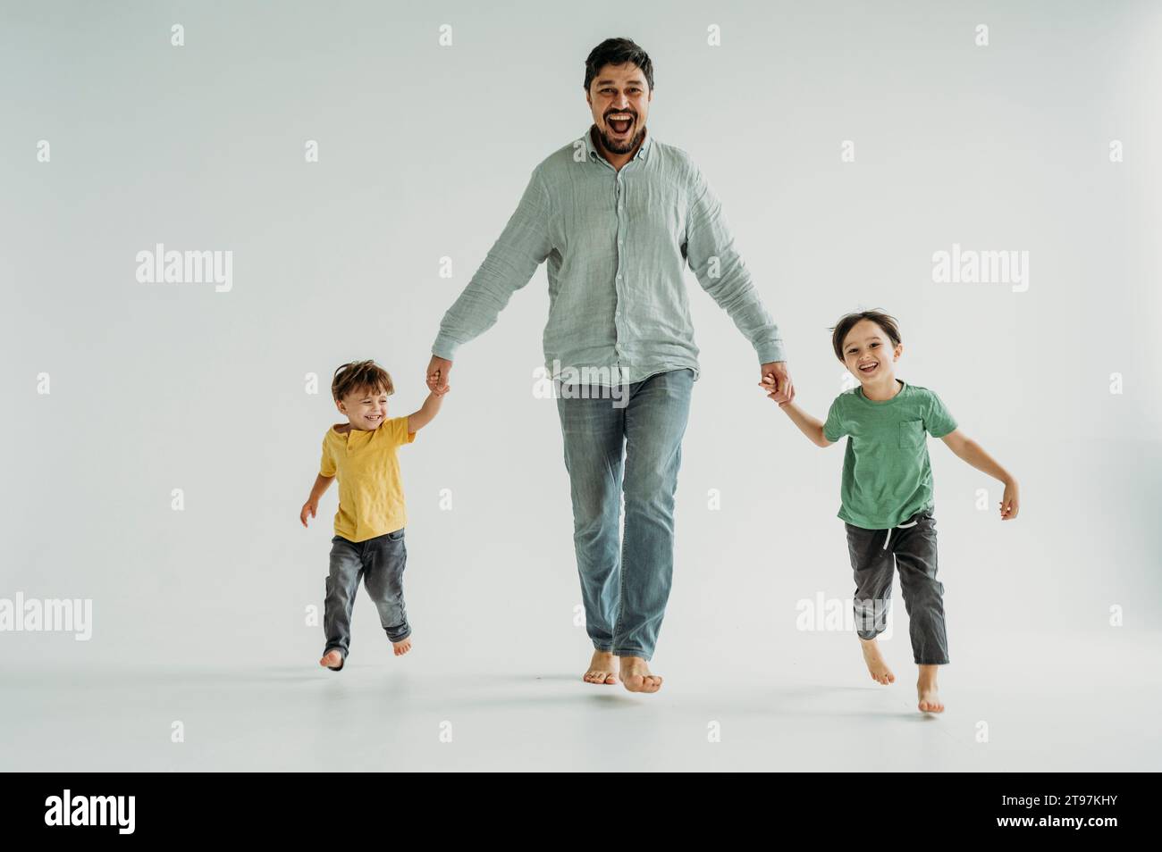 Happy father holding hands with children and running against white background Stock Photo