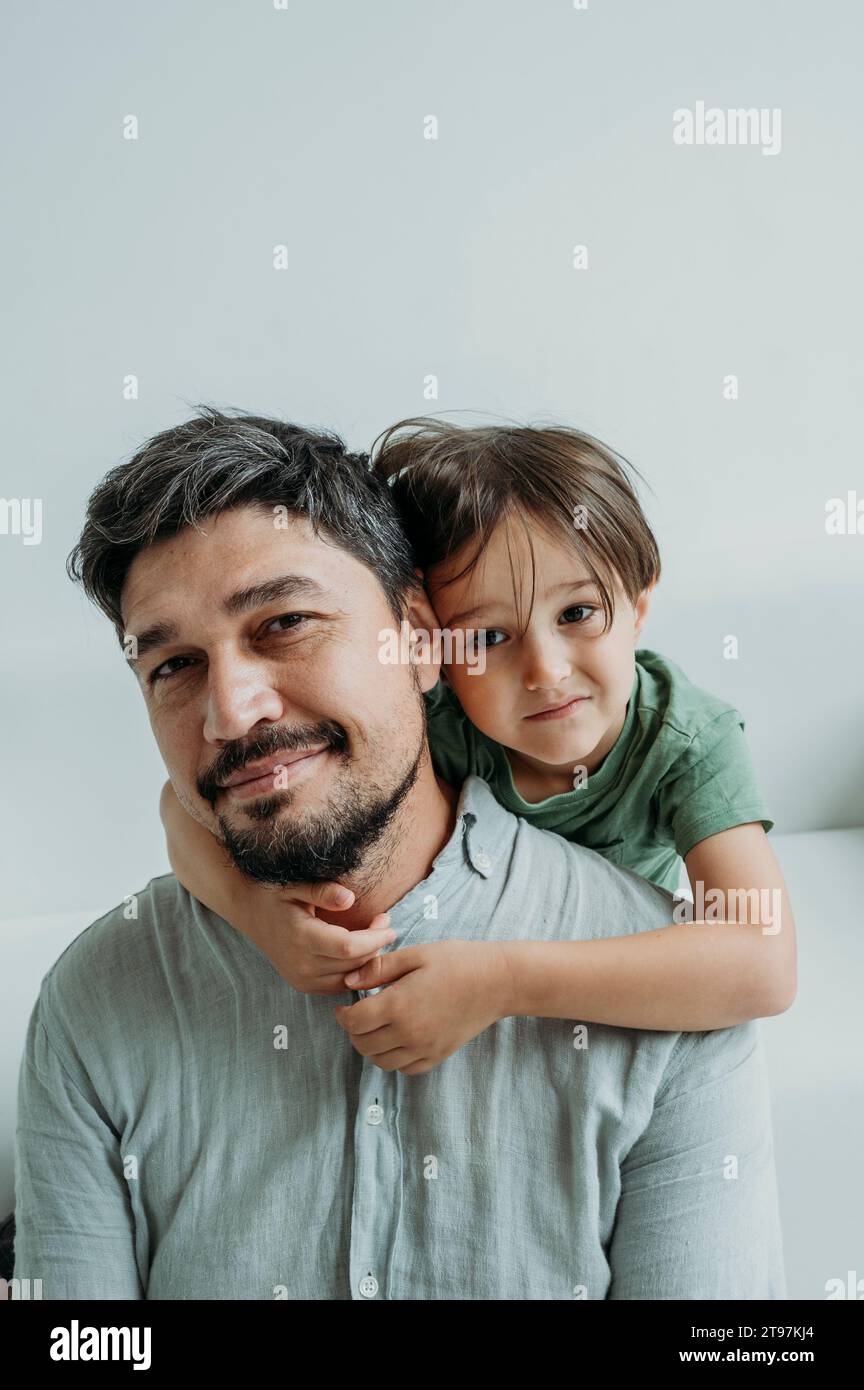 Smiling father sitting on sofa with son in front of white wall Stock ...