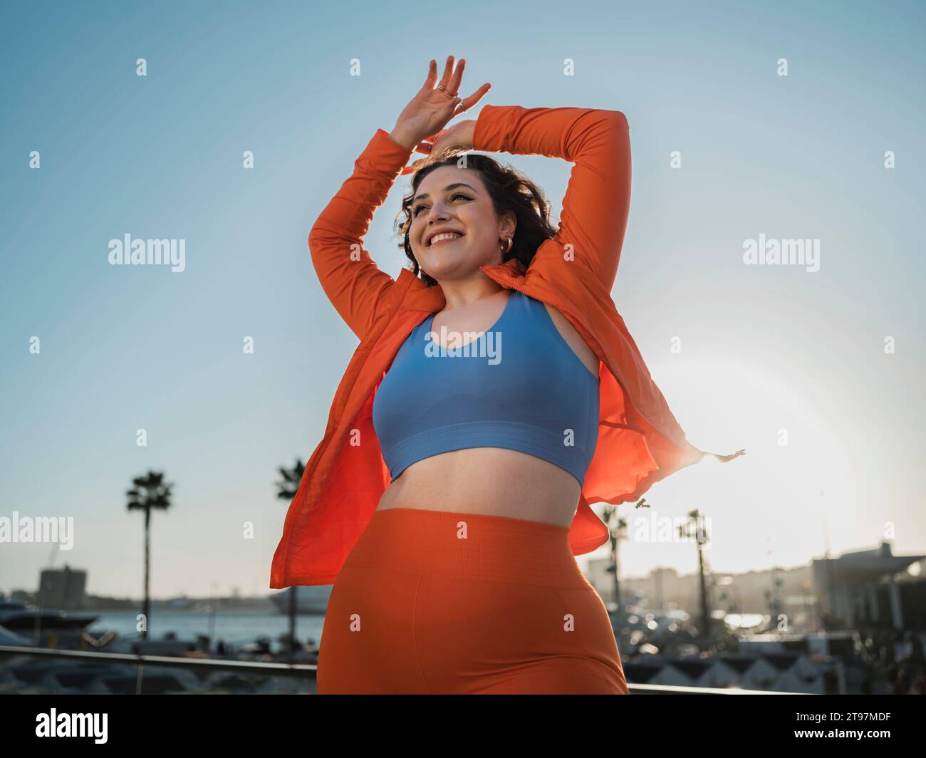 Happy woman in sports clothing standing with arms raised under sky Stock Photo