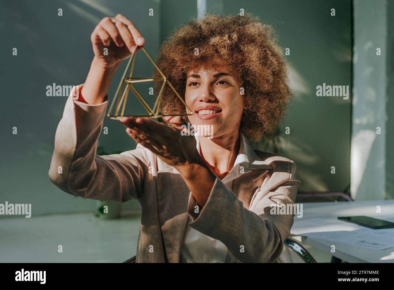 Happy businesswoman examining metal pyramid in office Stock Photo