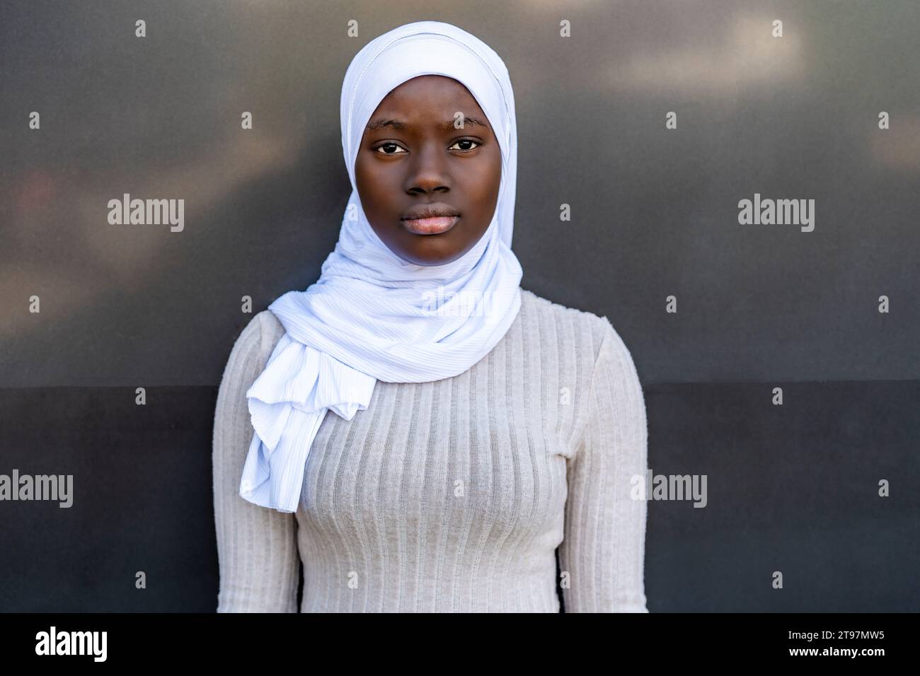 Young woman with hijab standing in front of gray and black wall Stock ...